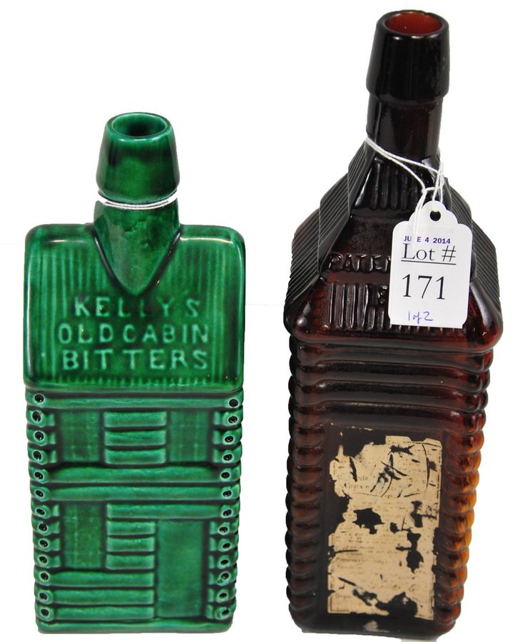 Two Bitters Bottles: One 10" cabin shaped amber bottle marked S T Drakes 1860 Plantation X Bitters, and one 9" green-glazed ceramic bottle marked Kelly's Old Cabin Bitters.