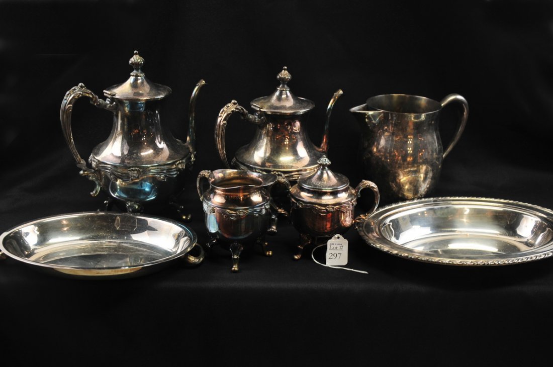 Mixed Silver Plate Serveware Lot: Includes a silver on copper set of two ornate teapots, creamer and footed sugar bowl with lid; also includes a large footed and handled serving tray, a water pitcher, and a covered serving dish.