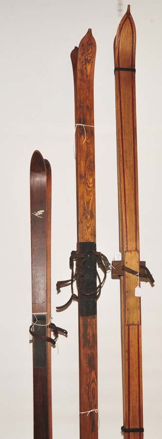 Three pair of old wooden skis: 83 1/2"L bordered red stripes, 80" L, and 58" L depicts a down hill skier signed on back 5' pine.