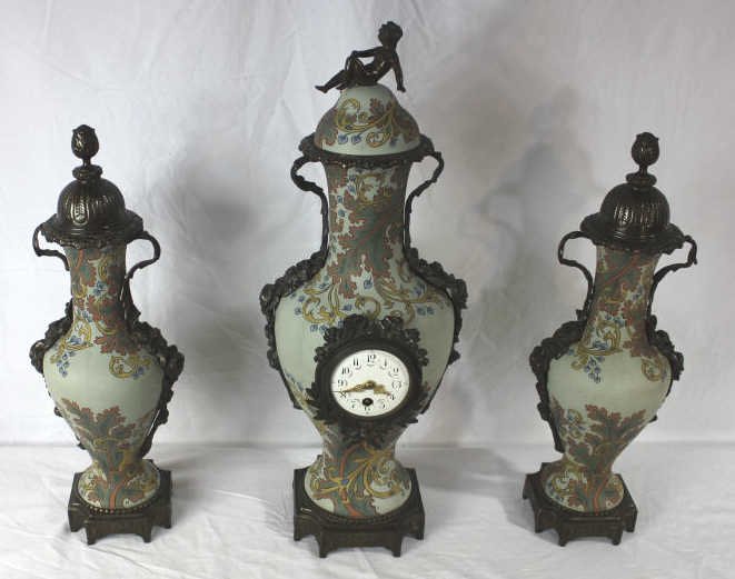 Three Piece Mettlach Clock Garniture Set. C. 1907.: The porcelain urns and clock case decorated in the Art Nouveau style The base interior of one of the urns with the Mettlach stamp date 1907 and 2414 model number. All having bronze mounts the clock wi