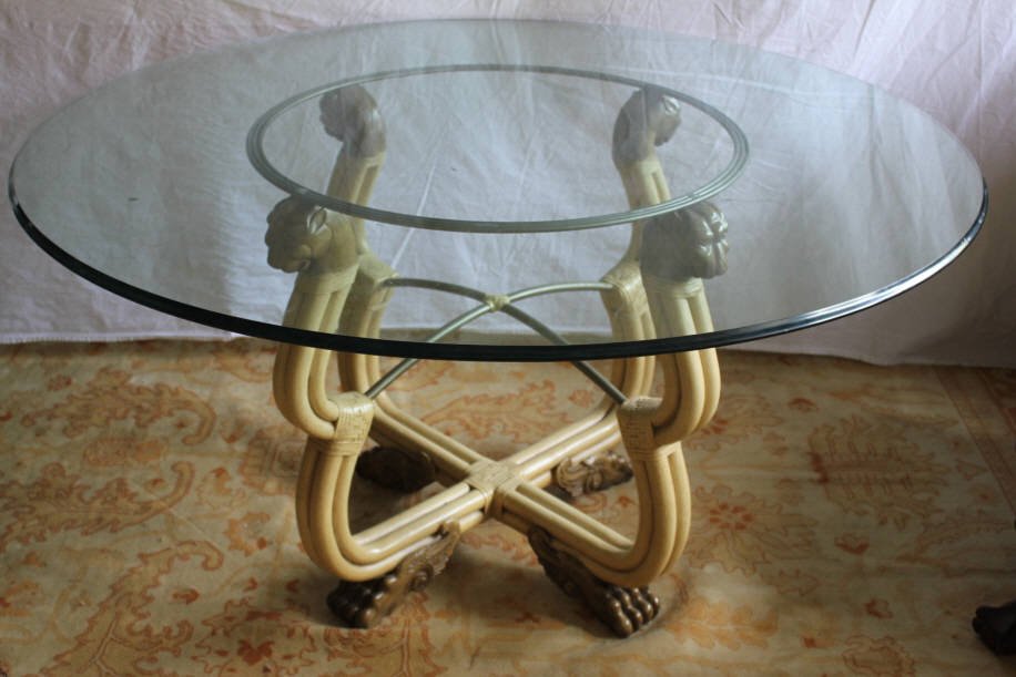Bamboo & Rattan Glass Top Dining Table: The round glass top supported on a rattan base with carved lion head finials and paw feet. Height 30 inches. Diameter of glass 50 inches. Property of a Bedford NY Home.