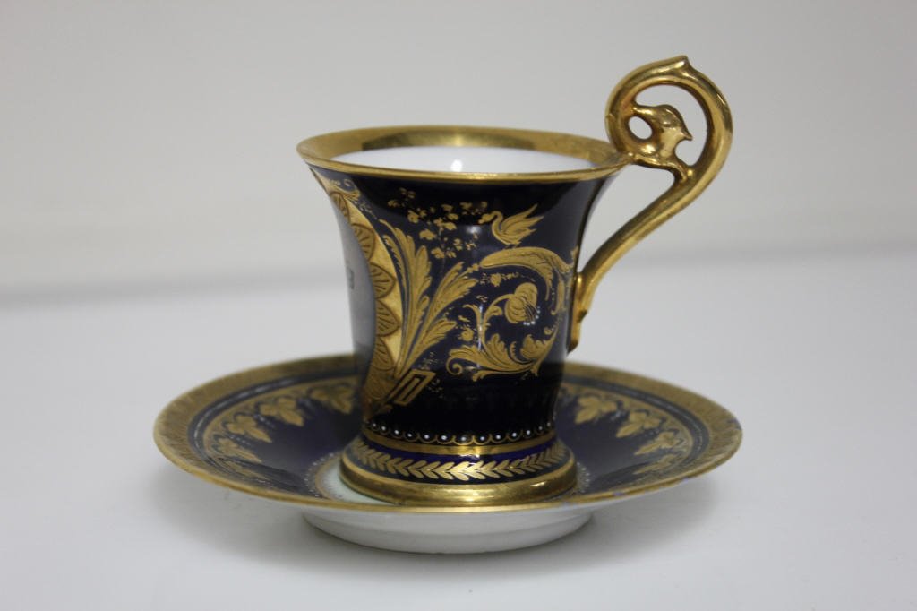 Royal Vienna Gilt & Royal Blue Cup and Saucer: with leaf motif. Featuring portrait of a woman. Cup height: 2.5 inches. Diameter: 2.25 inches. Plate height: .75 inches. Diameter: 4 inches. Hallmarked with beehive on cup and Saucer
