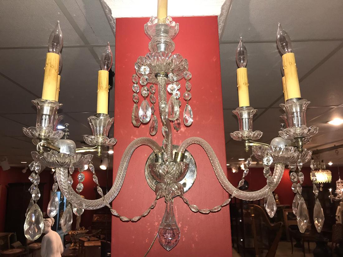 Antique Crystal Sconce: Possibly Waterford. With three branches wrapped in crystal having scalloped bobeche and floral inspired candle cups. Decorated with faceted beads and almond-shaped prisms. 26H x 26W x 12D.