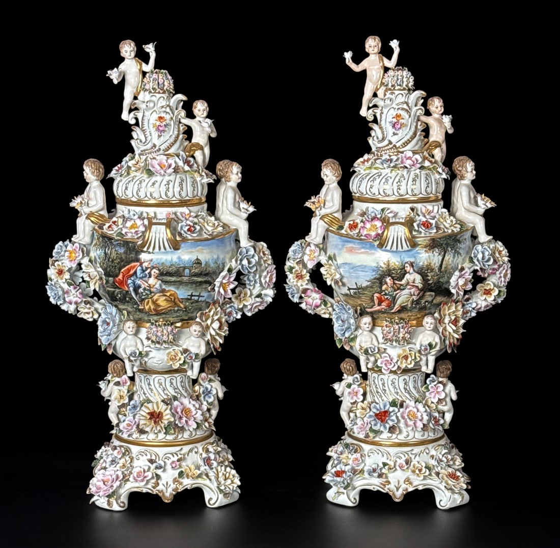 Pair Large Dresden Style Porcelain Urns: Pair Large Dresden Style Porcelain Urns, Each With Putti On Lids And Rims, Flowers Throughout, Bodies Painted With Courting Scenes, Height 27, Width 14, Depth 10 Inches, Structurally Sound And Present