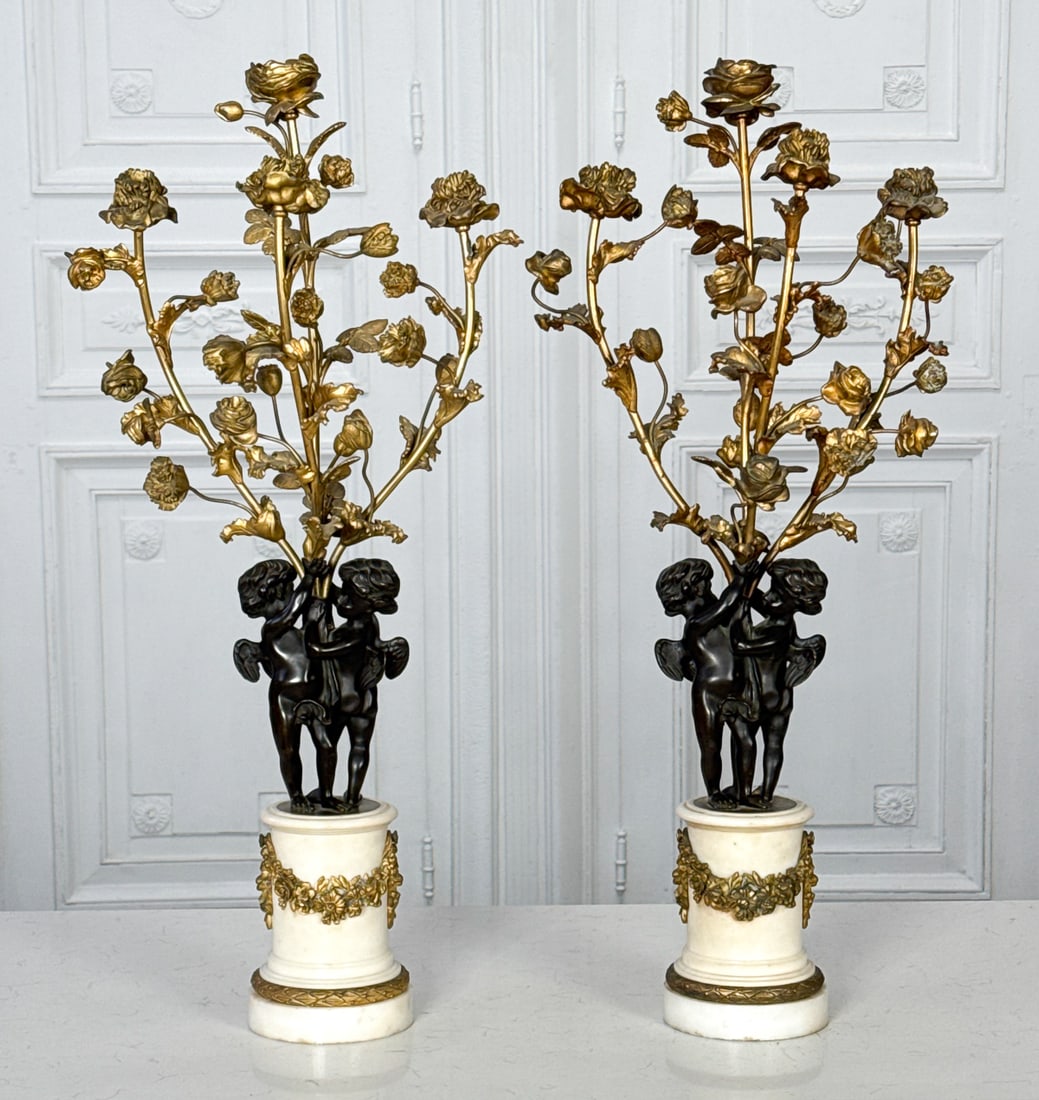 Pair Parcel Gilt Bronze & Marble Candelabra: Pair Parcel Gilt Bronze & Marble Candelabra, Probably French, Early 20th Century, Louis XVI Style, Each With Four Flower Form Lights Held By Two Winged Cherubs, Carrara Marble Bases, Drilled For Elect
