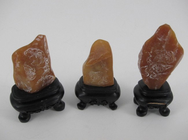THREE CHINESE CARVED SOAP STONE ITEMS ON STANDS: With relief decoration of hens under a tree on one and bats on the other two. Height 2-2.75" on wood stands.