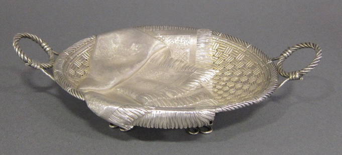 RUSSIAN SILVER BASKET: Punch marks with head of a woman and cyrillic letters. Pierced basket weave form with twin rope handles, with a draped trompe l'oeil chased fringed scarf with floral decoration. Raised on four silver