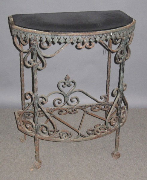 ANTIQUE WROUGHT IRON DEMI LUNE CONSOLE TABLE: A antique Demi Lune wrought iron two tier garden console table. The black glass insert top above a scroll works panel open conforming galleried lower shell. The whole resting on scrolled feet.17.25"x1