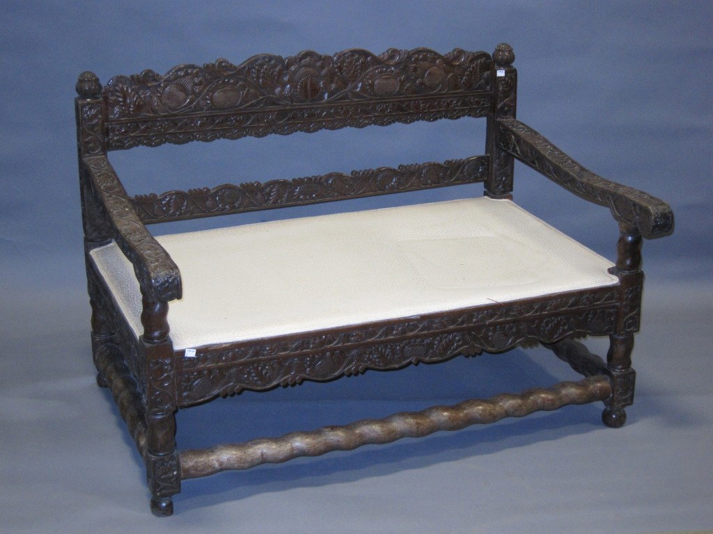 SETTEE AND ARM CHAIR: A 19th C. Anglo Indian elaborately carved dark patinated oak settee and matching open arm chair in an all over flowering vine motif each mounted with stylized finials. The settee measures 47" in lengt