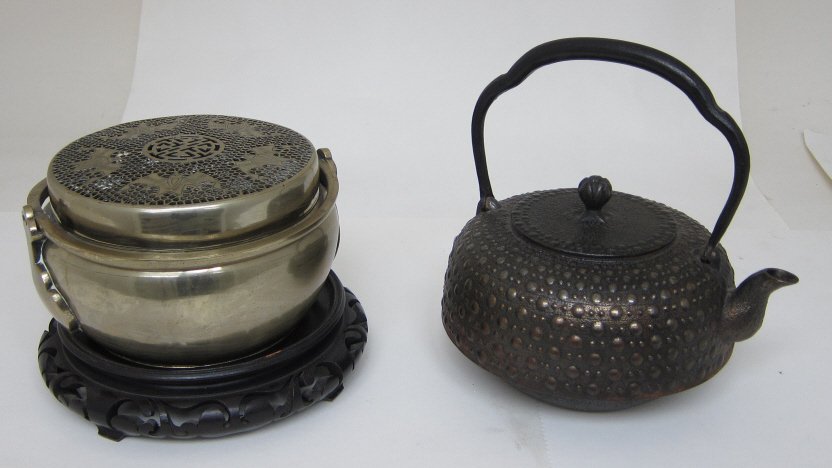 ORIENTAL TEAPOT AND BRAZIER: An iron teapot with raised knobs and lid with bud finial. Character marks on the bottom. W. and H. 8." Along with a brass round brazier with pierced lid with bat motifs and swing handle. Diam. 7." On 