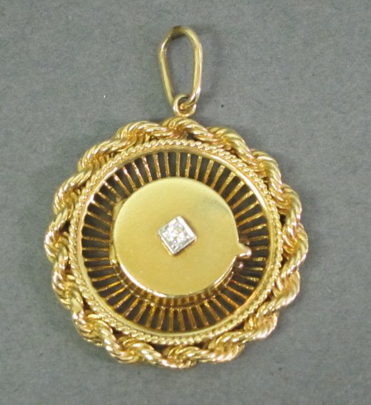 14K GOLD CHARM WITH DIAMOND: Yellow gold circular form with central medallion locket set with a single diamond. 18 grams.