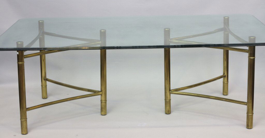 DINNING TABLE: A contemporary glass top dinning table. The rectangular top,having rounded corner,resting on twin brass triangular tubular pedestals 84" L x 48" W x 29" H
