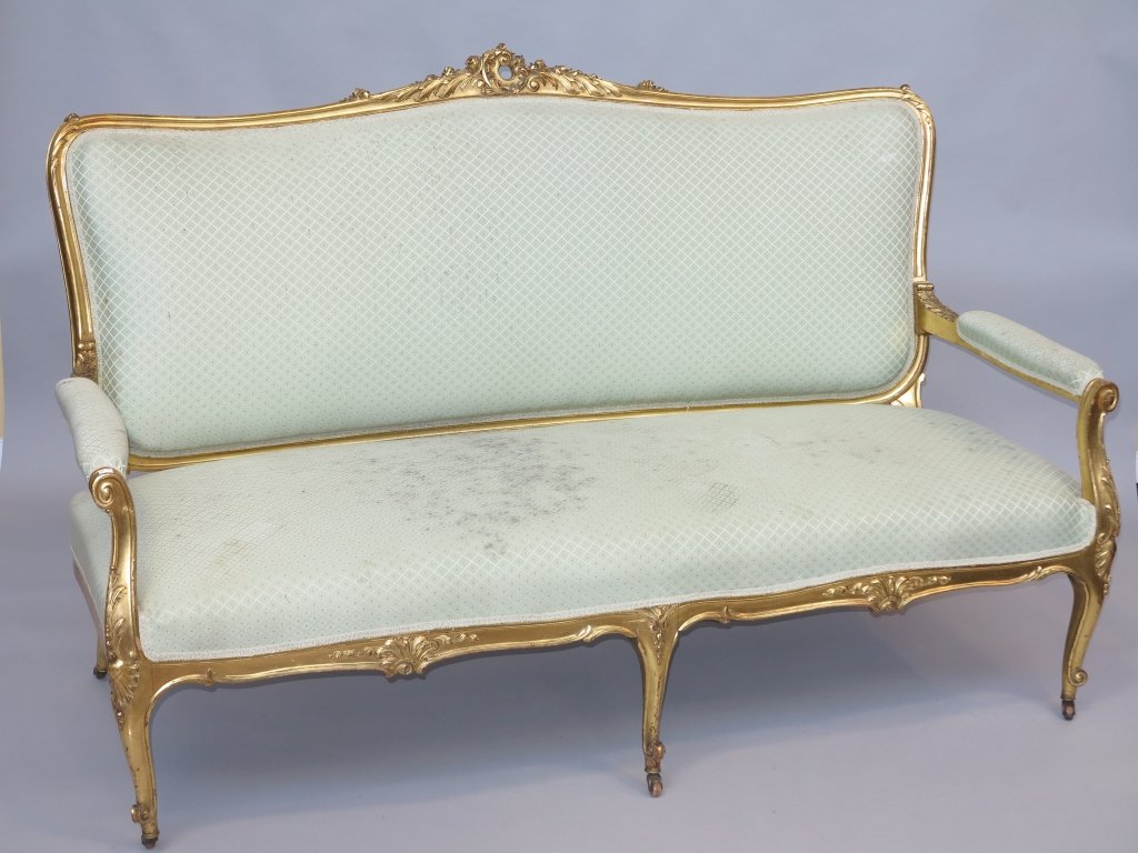 SETTEE: An antique French Louis XV style carved and gilt salon settee. The rectangular curved back, having a rococo style pierced crest before curved arms over a padded seat raised on curved legs terminating 