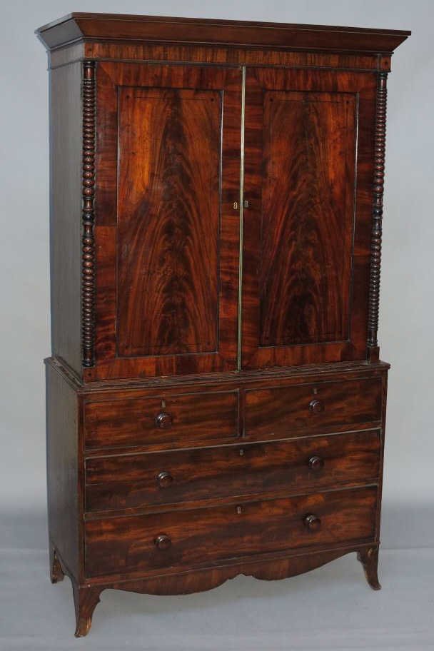 LINEN PRESS CABINET: A 19th century English Georgian style mahogany linen press cabinet, the moulded cornice above double cabinet doors centered by spool turned flush columns over two short drawers, the whole raised on sp