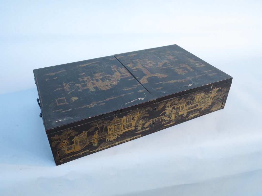 ANTIQUE ORIENTAL LACQUERED LAP DESK: Black with gilt decoration of figures in gardens with pavilions. The double hinged lid opens up to a compartment over a lower drawer. With escutcheons and metal carry handles. One half of the lid crac