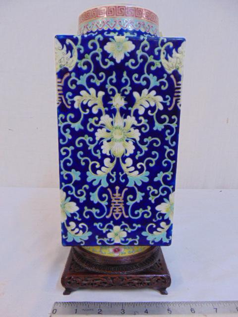 Square porcelain Chinese vase, decorated with various: Square porcelain Chinese vase, decorated with various flowers on blue field, on carved wood base, vase is 5" by 5", 11" tall