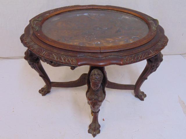 Oval carved top side table, glass tray top, figural: Oval carved top side table, glass tray top, figural carved legs, table has carved top showing nude in boat, table is 27.5" by 22", height is 20"