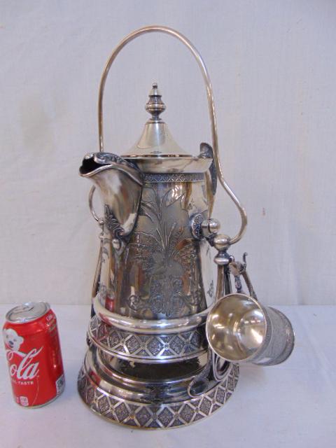 Ornate silver-plate ice water pitcher on stand with: Ornate silver-plate ice water pitcher on stand with cup, floral designs, pitcher pivots on stand, height is 18", 19th Century, interior lined with porcelain.