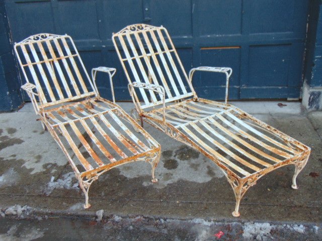Pair iron chaise lounges by Woodard, white paint,: Pair iron chaise lounges by Woodard, white paint, rust is visible, with wheels on head end, iron patio or pool furniture.