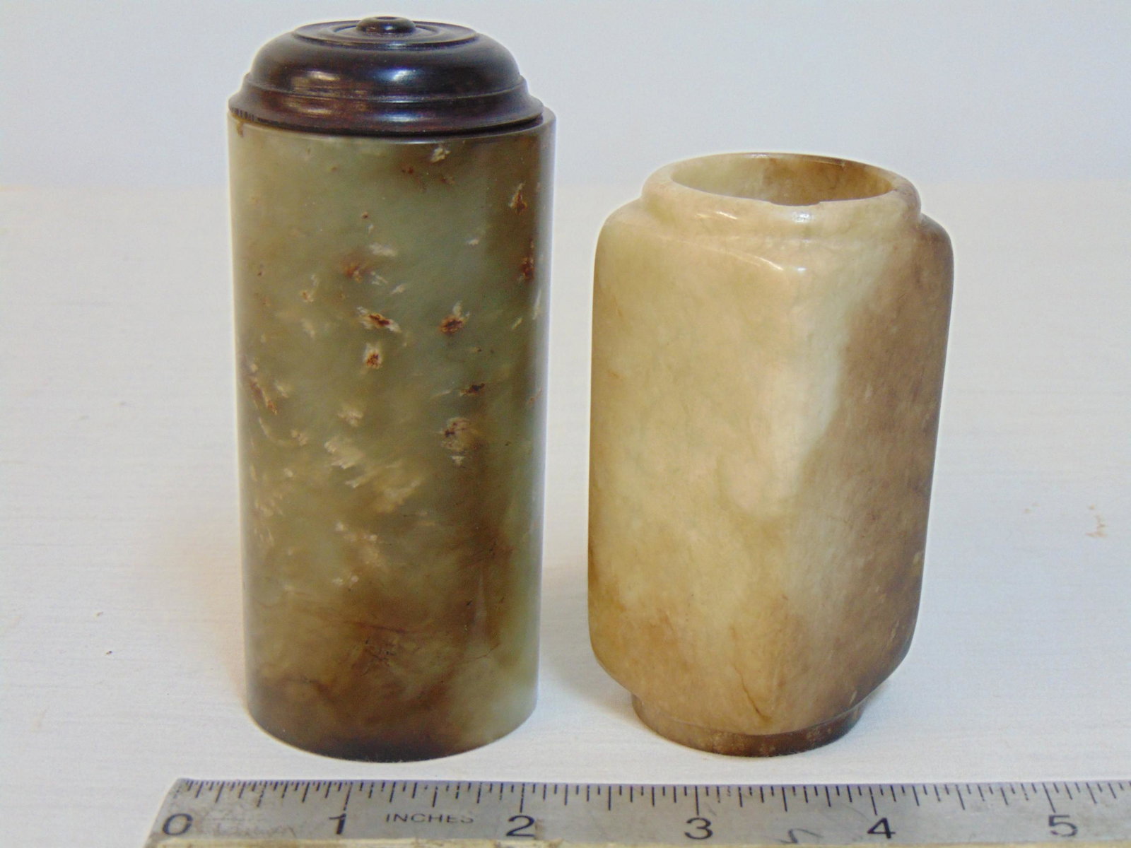 2 carved Chinese jade vessels, cylindrical & square shaped, square shaped jar is 3 3/8" tall, 1.5": 2 carved Chinese jade vessels, cylindrical & square shaped, square shaped jar is 3 3/8" tall, 1.5" wide, 1 5/8" deep, has small chip top edge, cylindrical jar with wood lid, vessel is 3 7/8" tall, dia