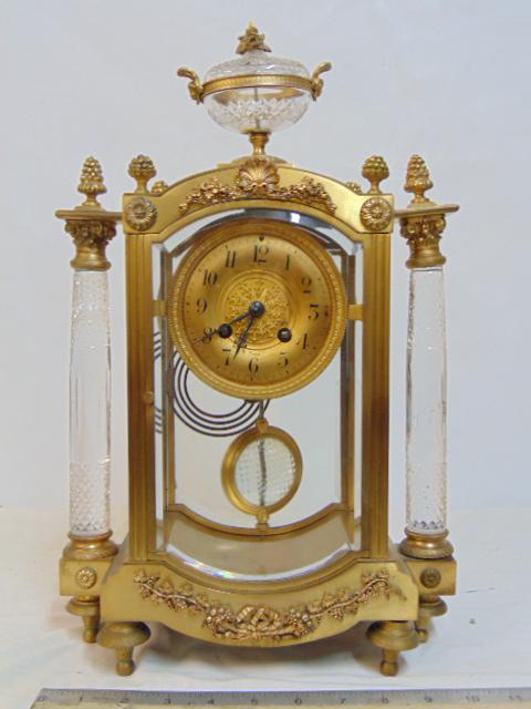 Le Roy crystal & brass mantle clock, with two cut crystal columns & crystal pendulum, finial,: Le Roy crystal & brass mantle clock, with two cut crystal columns & crystal pendulum, finial, columns are chipped, rear leg slightly bent, clock is 16.75" tall, 10.5" wide, depth is 5.25"