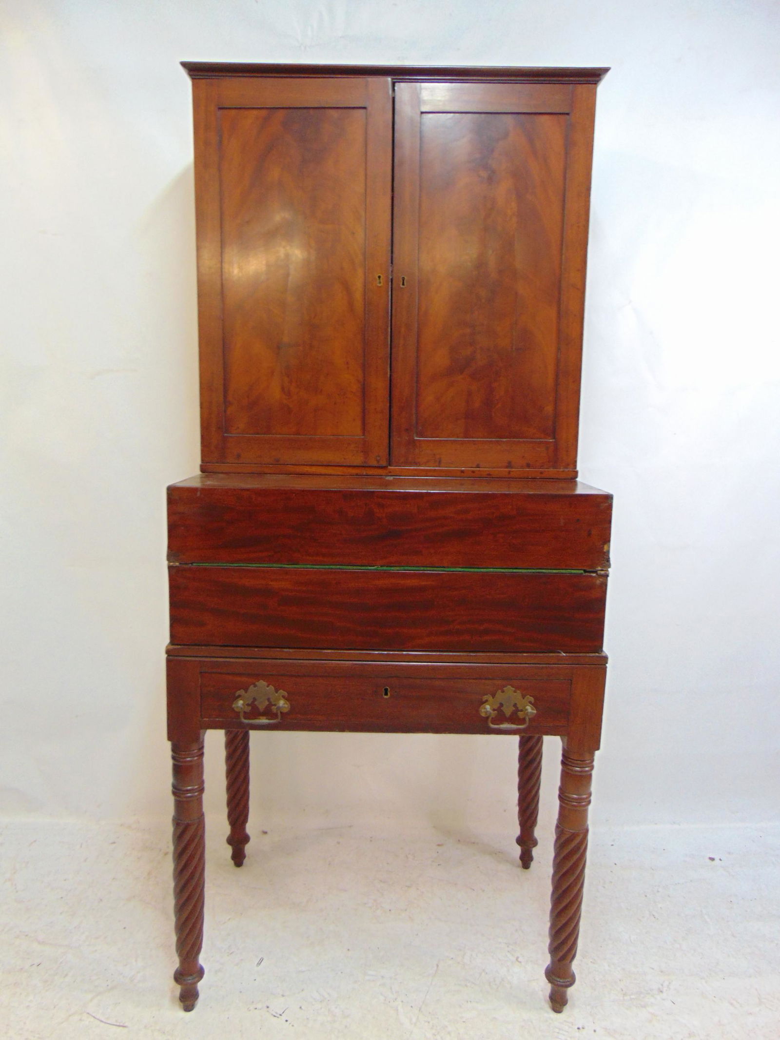 Sectional desk, in mahogany, campaign style, consists of three pieces, base with drawer, center: Sectional desk, in mahogany, campaign style, consists of three pieces, base with drawer, center section with fold out desk, & top section with two doors & shelves, desk, as shown is 28.5" by 19.5", he