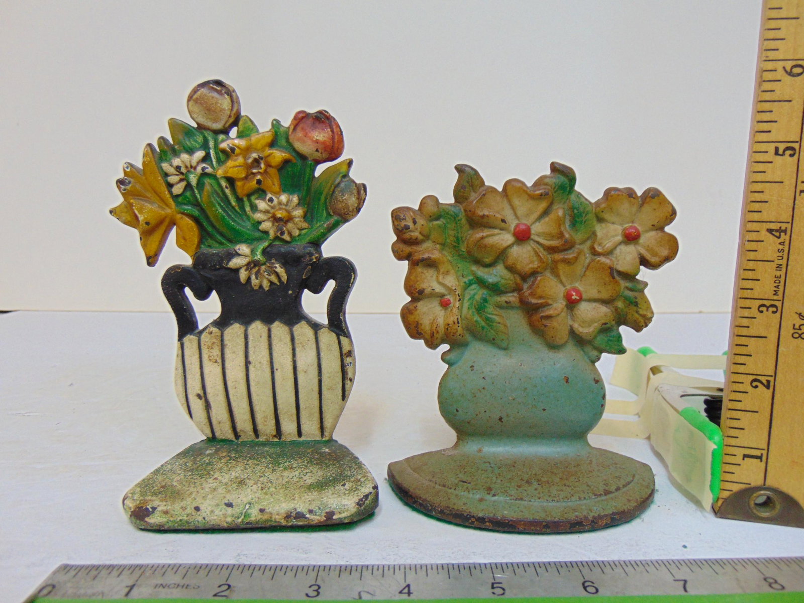 2 small cast iron floral doorstops, one in black & white vase, one with white flowers, 4 7/8" and: 2 small cast iron floral doorstops, one in black & white vase, one with white flowers, 4 7/8" and 6.25" tall.