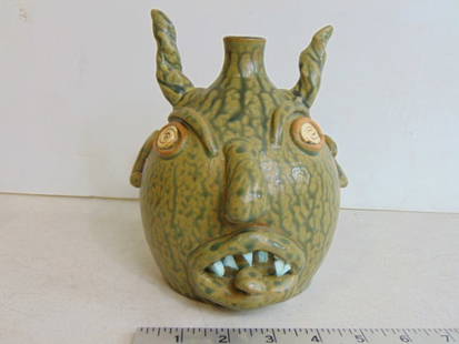 Small devil face jug by Leftwick Folk Art Pottery, marked KIM, in green with dark accents, spiral: Small devil face jug by Leftwick Folk Art Pottery, marked KIM, in green with dark accents, spiral eyes, height is 7", dated 2001