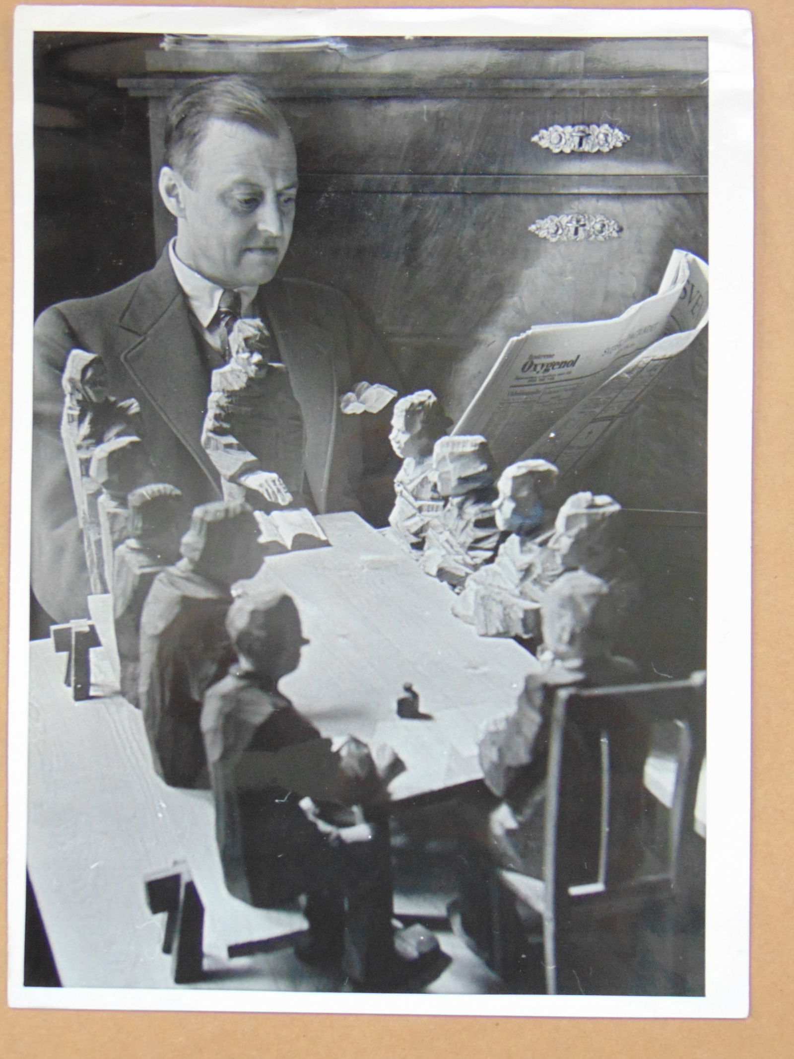 Photograph, attributed to Alfred Eisenstaedt, "Upsala, March 1934", unidentified manreading a paper: Photograph, attributed to Alfred Eisenstaedt, "Upsala, March 1934", unidentified manreading a paper superimposed over a wood carved installation of figures around a table, with early German Associated