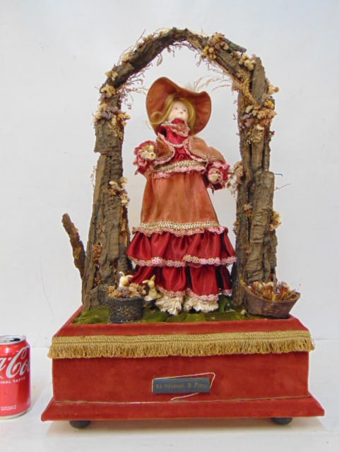 Automaton, "La Vendeuse A Fleurs", girl under rustic arch, velvet base, made in Belgium, 1997 label,: Automaton, "La Vendeuse A Fleurs", girl under rustic arch, velvet base, made in Belgium, 1997 label, base is 15.75" by 9.5", height is 26", no key, working condition unknown.
