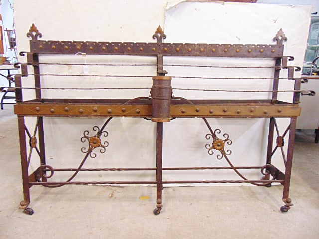 Church devotional votive candle stand in wrought iron, collection box in center, all candle cups are: Church devotional votive candle stand in wrought iron, collection box in center, all candle cups are removed, 65" long, 12" deep, height is 42 5/8", base has floral decoration, one caster is missing.