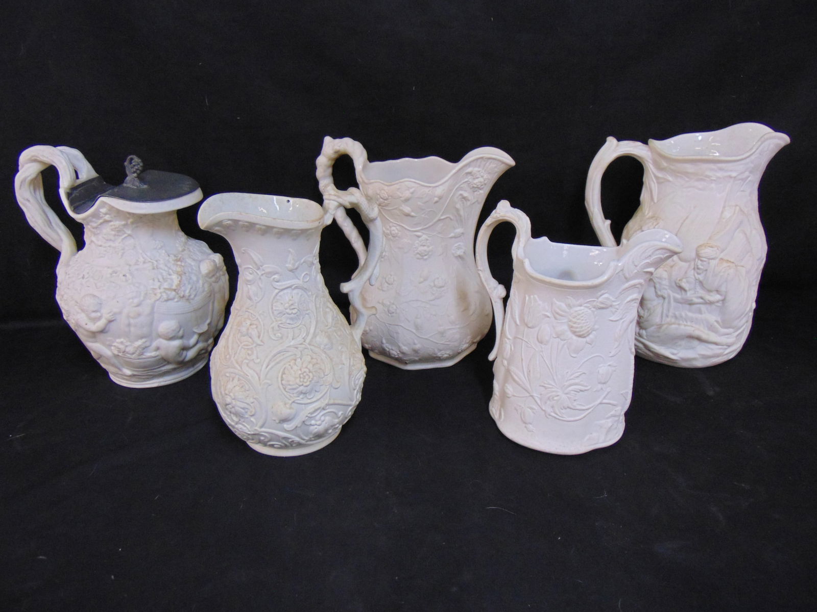 5 Parian & relief molded pitchers, two are repaired, one is missing Pewter lid, tallest one is: 5 Parian & relief molded pitchers, two are repaired, one is missing Pewter lid, tallest one is 10.25".