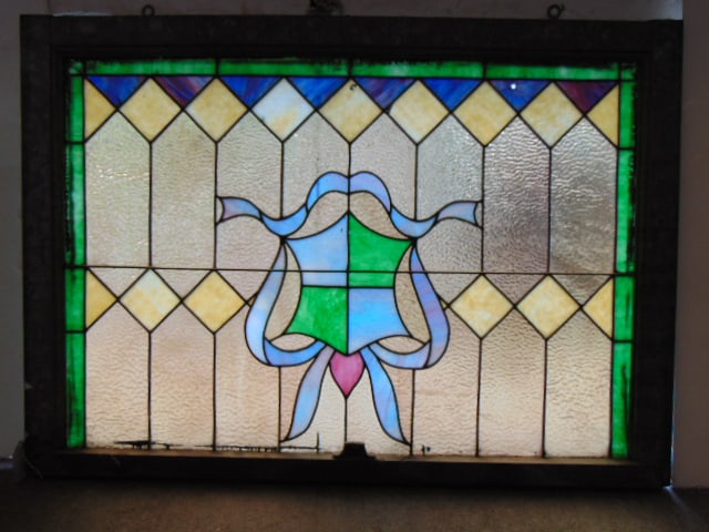 Leaded glass window with armorial shield, ribbon decorations, window is 31" by 44", one blue: Leaded glass window with armorial shield, ribbon decorations, window is 31" by 44", one blue triangle piece has small hole.