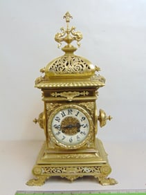 Ornate brass mantle clock, decorated with various winged creatures, griffins, porcelain dial, finial