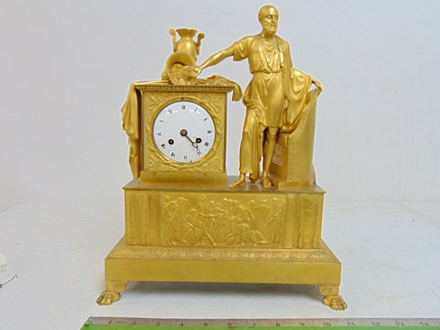 Antique gilt bronze Empire mantle clock, classical decoration with figure and urns, one on it's side: Antique gilt bronze Empire mantle clock, classical decoration with figure and urns, one on it's side with coins spilling, pendulum, key holes have chips, clock is 11.75" wide, 5.25" deep, height is 14