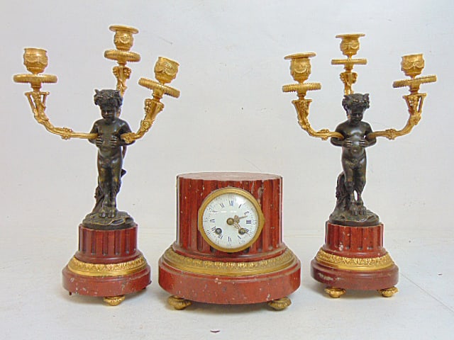 3 piece marble & bronze clock set, column shaped red marble clock & figural bronze & red marble: 3 piece marble & bronze clock set, column shaped red marble clock & figural bronze & red marble garniture, candelabra, clock is missing one foot, both candelabras are missing a foot, height candelabra