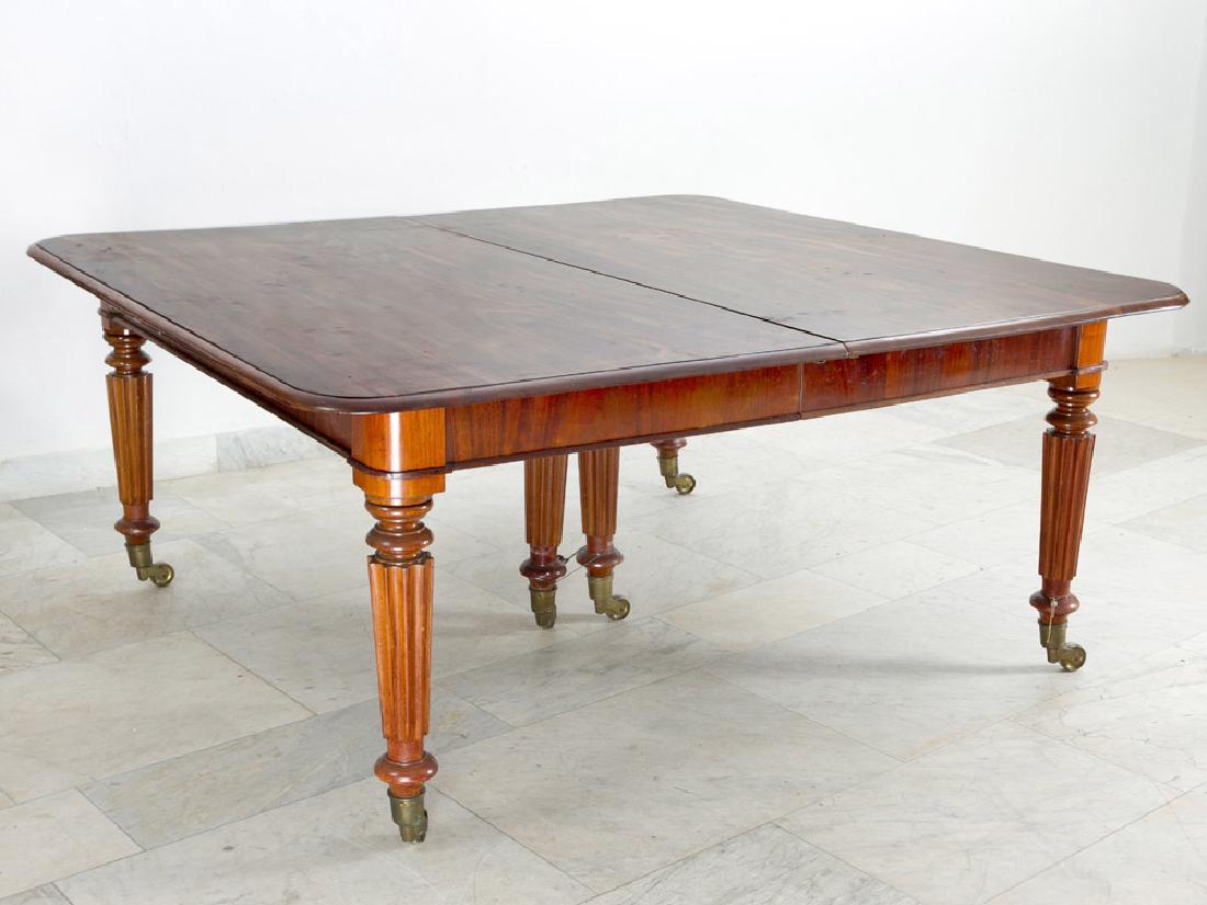 A large extendeble Victorian dinning table: A large extendable Victorian dinning table on six flutted and turned concave legs on bronze wheels; round corners and vertical verneered frieze; the top with round stepped border and as well rounded c