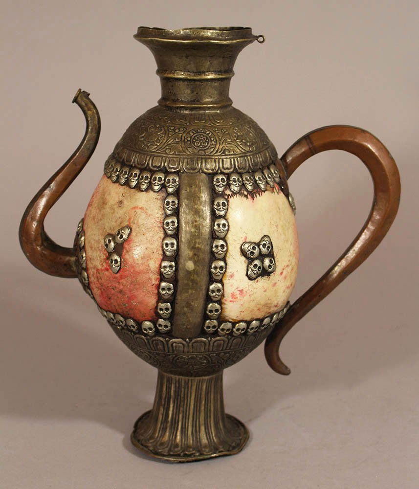 Asian or Oceanic Cultural Jug with an Ostrich egg in: Asian or Oceanic Cultural Jug with an Ostrich egg in the centre and skull decorations in silvered and chased copper mount , handgrip and spout, fluted round column base , upper round border with a rin