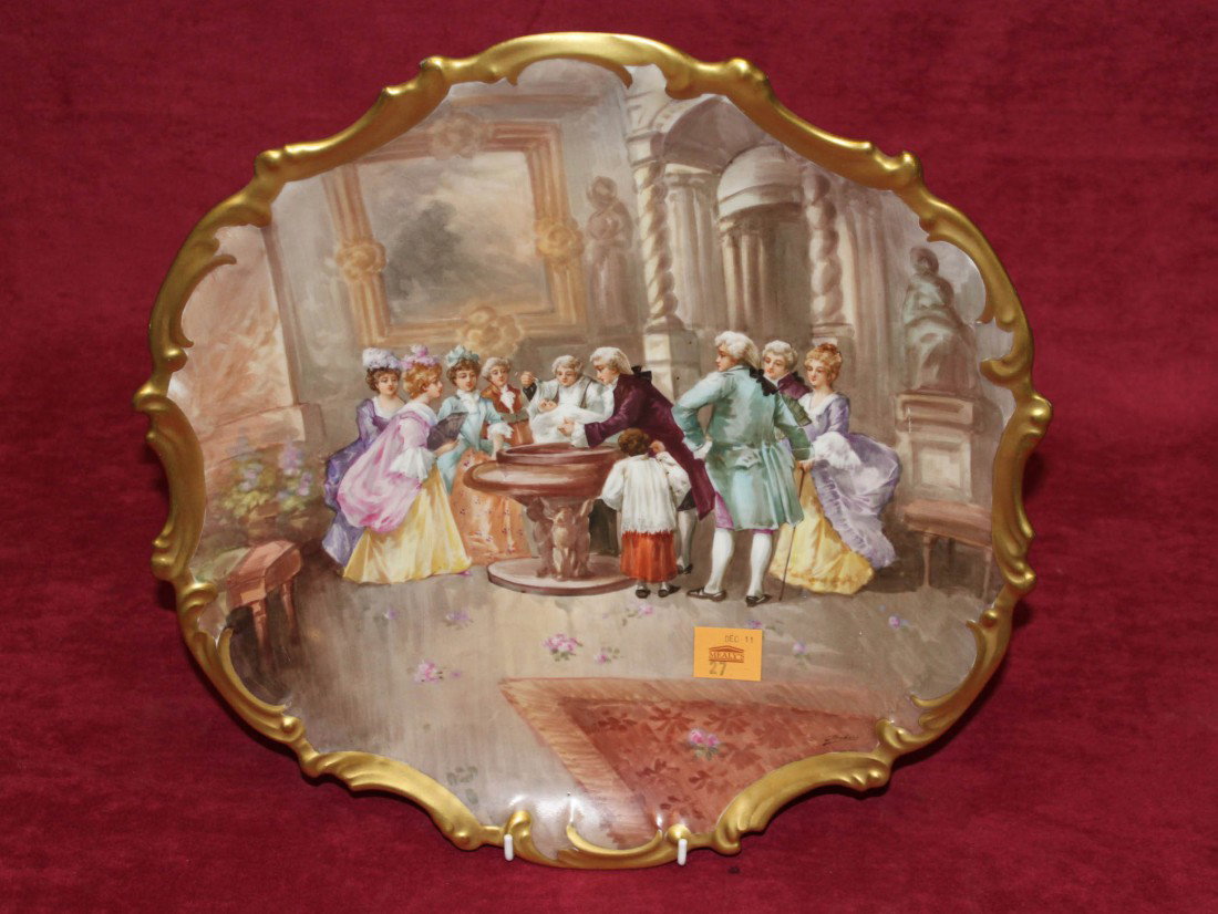 A large Limoge porcelain Wall or Cabinet Dish, deco: A large Limoge porcelain Wall or Cabinet Dish, decorated with elegant figures in a stately room with cleric baptising a child in a fountain inside a scroll gilt edge, 15 14" (39cms), signed Dubois. (1