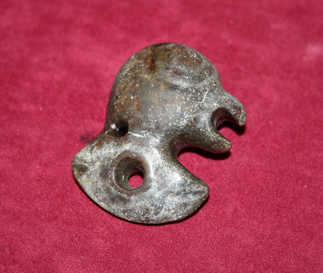 An archaic carved dark Jade pendant in the form of: An archaic carved dark Jade pendant in the form of a chicken head, with two perforations, 2" (5cms)