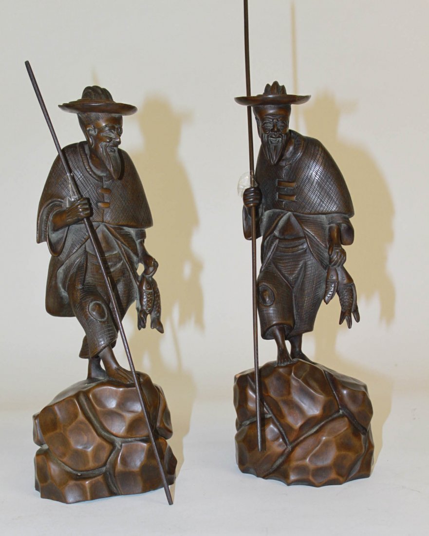 A pair of carved Chinese figures, each modelled as: A pair of carved Chinese figures, each modelled as a fisherman holding fish in left hand and spear in the other, 12.5" (32cms). (1).