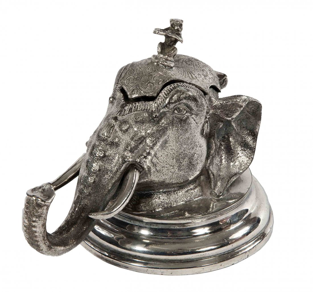 An Indian silver plated elephant head ink stand, l: An Indian silver plated elephant head ink stand, late 19th century, the hinged cover surmounted with a monkey, 8'' (20cms). (1).