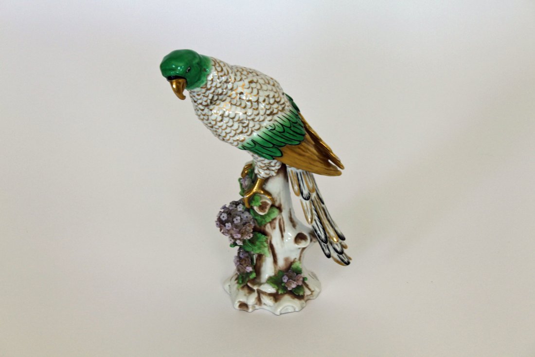 A Continental porcelain model of a Parrot, : A Continental porcelain model of a Parrot, circa 1900, modelled perched on a tree-stump above a pompom of flowers, its plumage enriched in green, white, gilt and black (some minor chipping), 11"h (28c