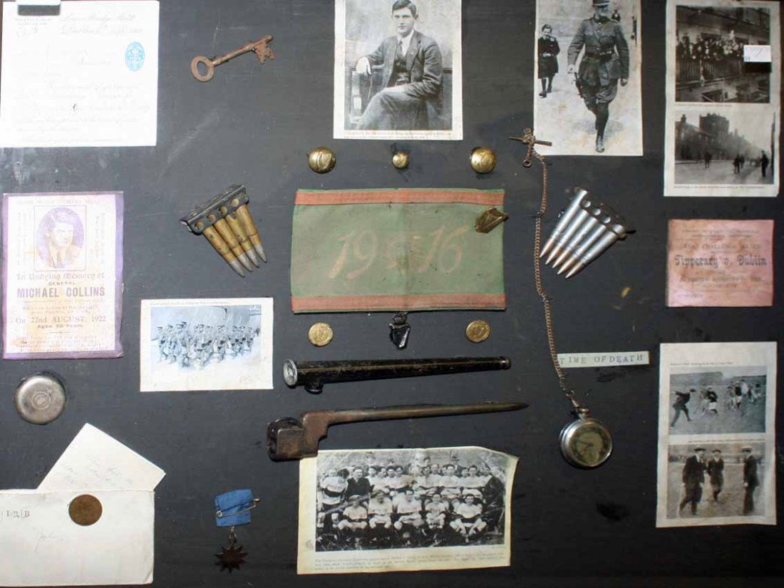 A FACSIMILE FRAMED COLLECTION OF MICHAEL COLLINS: A FACSIMILE FRAMED COLLECTION OF MICHAEL COLLINS MEMORABILIA, containing spike bayonet, mans pocket watch, bullets, buttons, key and various images etc., in framed display case, 23in (59cm)h x 30in (7