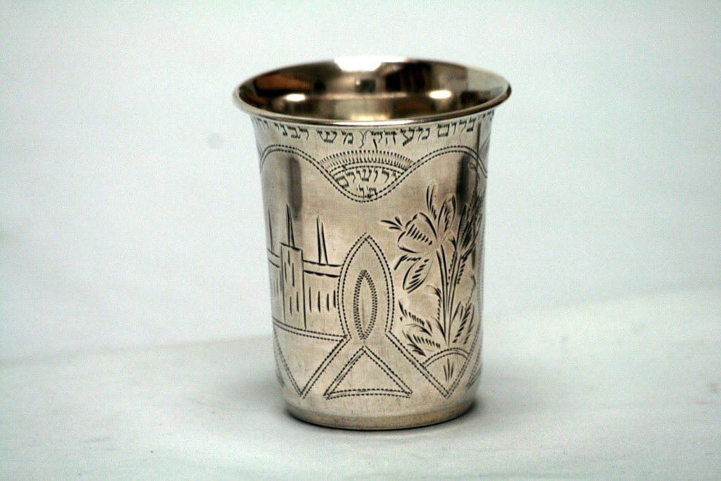 A LARGE HEBREW ENGRAVED JUDAICA KIDDUSH CUP.: Russia, c. 1900. Of traditional form. Designed with houses and town scene. Engraved in Hebrew "TO MY SON YECHEZKEL AND HIS WIFE LIPSHA, FROM YOUR DAD AVRHAM ELI BLOOM, FROM THE HOLY CITY OF JERUSALEM"