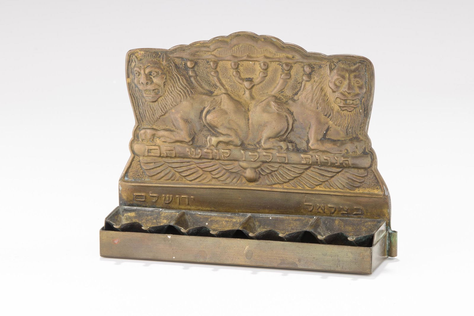 A BRASS HANUKKAH LAMP BY THE BEZALEL SCHOOL. Jerusalem, c. 1920. On four supports. The backplate (1 of 1)