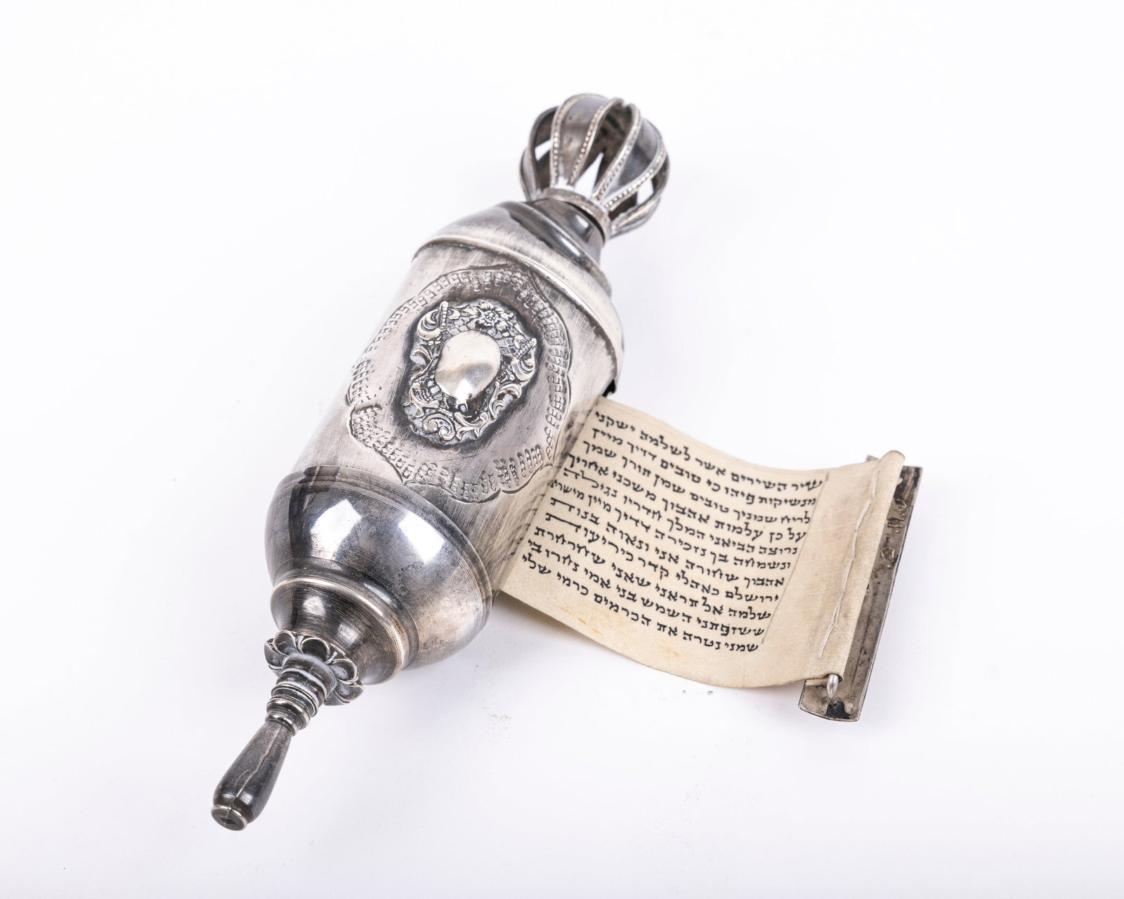 A SILVER SHIR HASHIRIM MEGILLAH CASE. Chased with central cartouche and topped with a crown. With: A SILVER SHIR HASHIRIM MEGILLAH CASE. Chased with central cartouche and topped with a crown. With Shir Hashirim scroll inside. Bend to the upper portion. 7.3" tall.