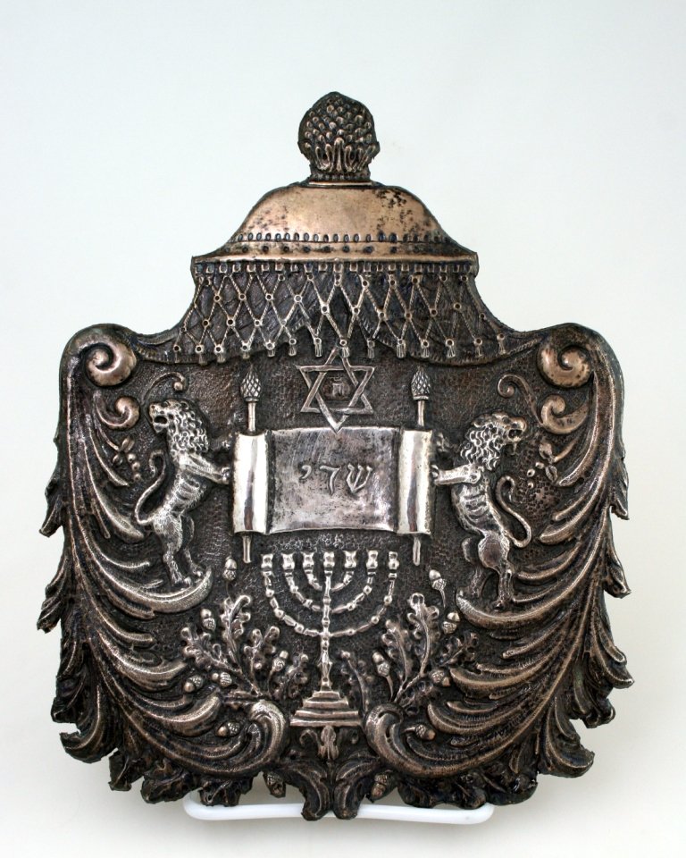 A SILVER TORAH SHIELD. Continental, 20th century.: A SILVER TORAH SHIELD. Continental, 20th century. Hand chased with two lions flanking a Torah, a temple style menorah and organic designs. 9.5” tall.