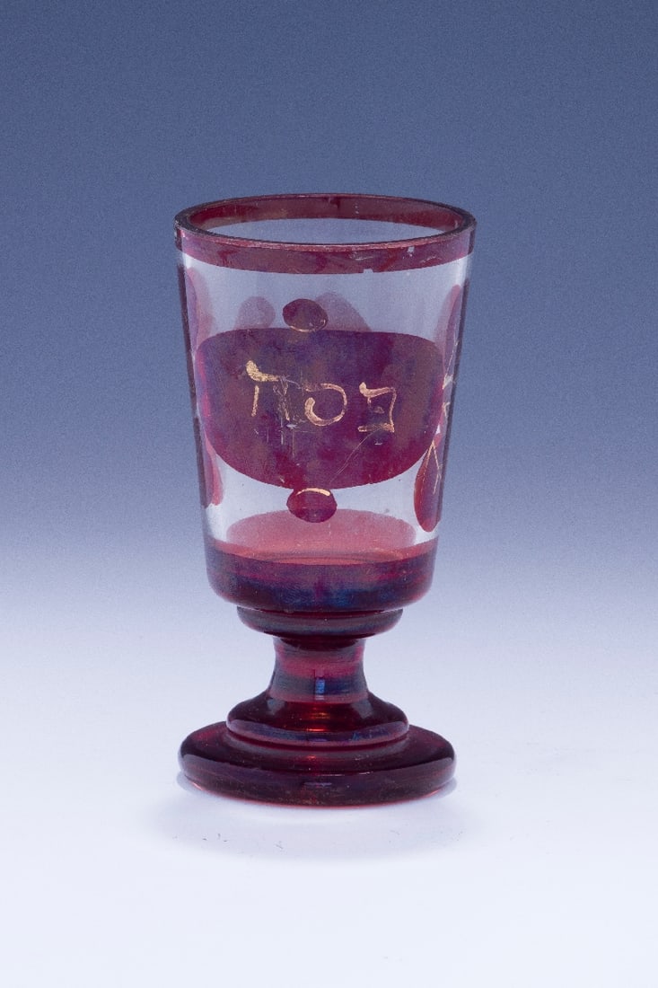 A GLASS PASSOVER CUP. : Poland or Germany c. 1880. Ruby colored glass with gold leaf design. Passover use indicated in central cartouche. One small chip is evident. 4.5" tall. Estimate $700 - 900