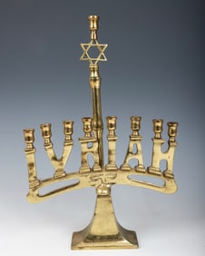 A BRASS IVRIAH MENORAH. American, c. 1940. On a tapering rectangular base. With the original servant